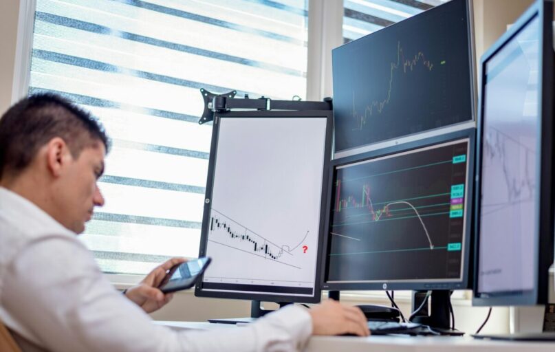 A stock trader analyzes financial data on multiple computer screens in an office setting.