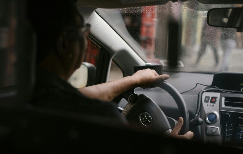 Back view of crop anonymous man in eyeglasses driving car in rainy day