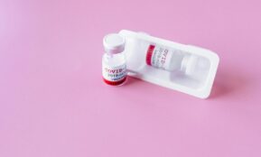 Close-up of COVID-19 vaccine vials on a pink surface, symbolizing healthcare and immunization.