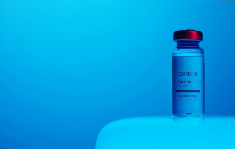 A COVID-19 vaccine vial with clear labeling on a serene blue background, symbolizing hope and health.