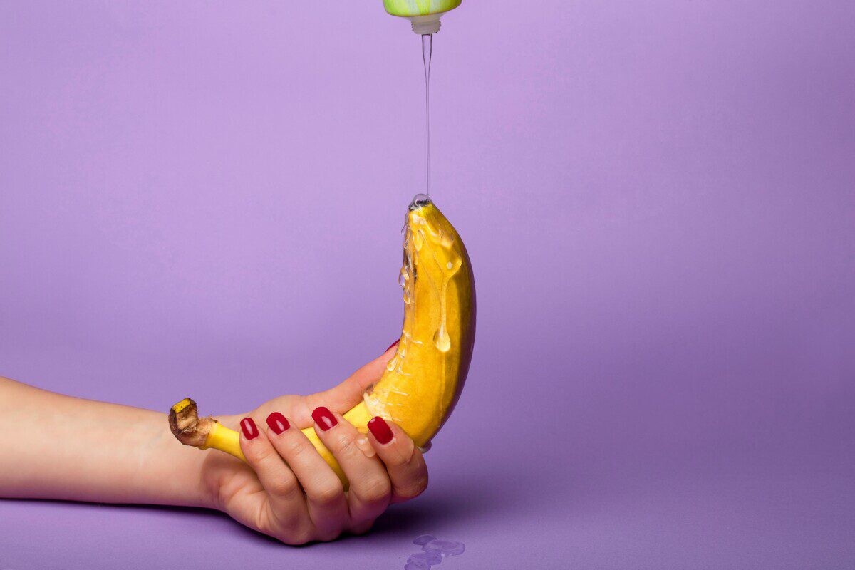 Vivid photo of a hand holding a banana with syrup pouring over it against a purple background.