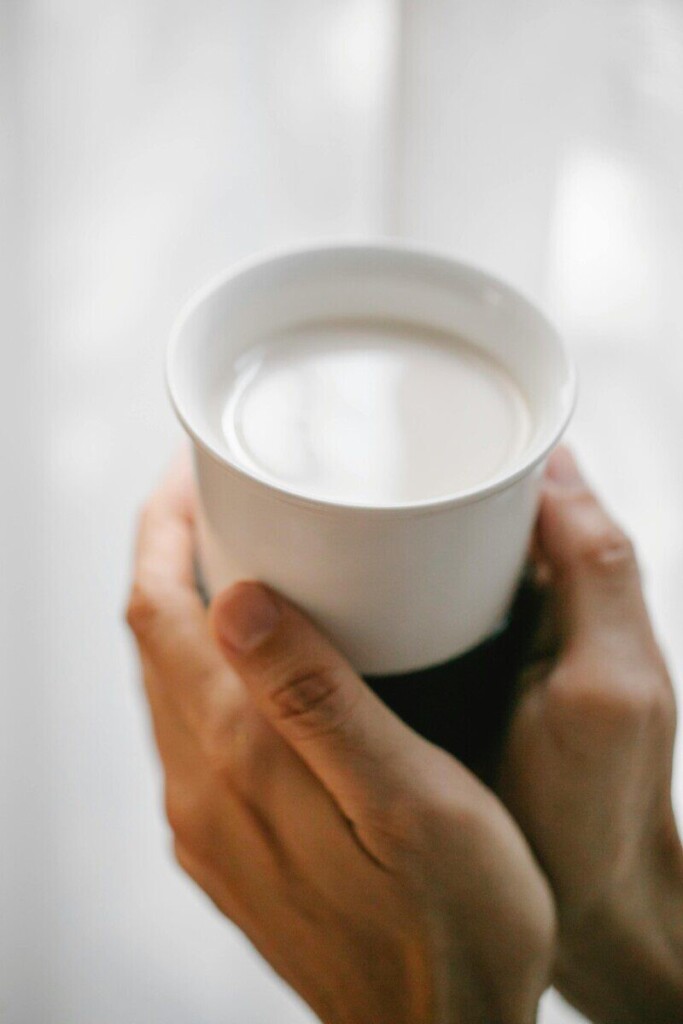 A comforting hand holding a ceramic cup filled with a creamy drink.