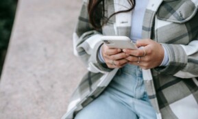 A woman using her smartphone while sitting outdoors, showcasing modern lifestyle and connectivity.