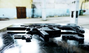 Various firearms displayed on a scratched metal table in an industrial setting.