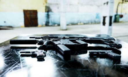Various firearms displayed on a scratched metal table in an industrial setting.