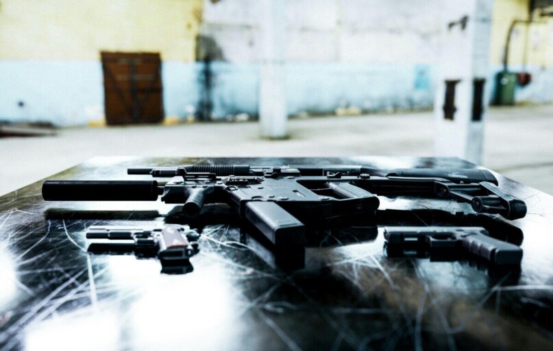 Various firearms displayed on a scratched metal table in an industrial setting.