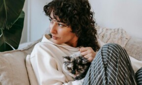 Adult contemplative female embracing cute cat while sitting on soft couch and looking away in living room