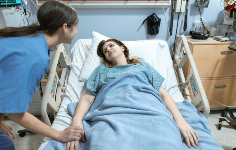 A nurse compassionately holds a patient's hand in a hospital room setting, promoting care and support.