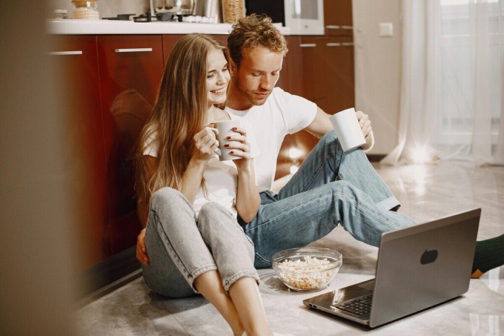 Young couple enjoying a cozy moment with popcorn and coffee by the computer at home.