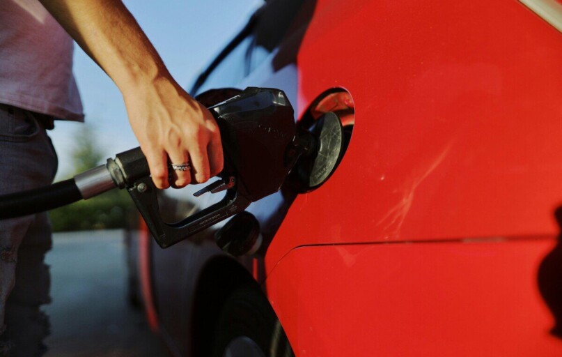 Close-up of a person refueling a red car at an outdoor gas station during the day.