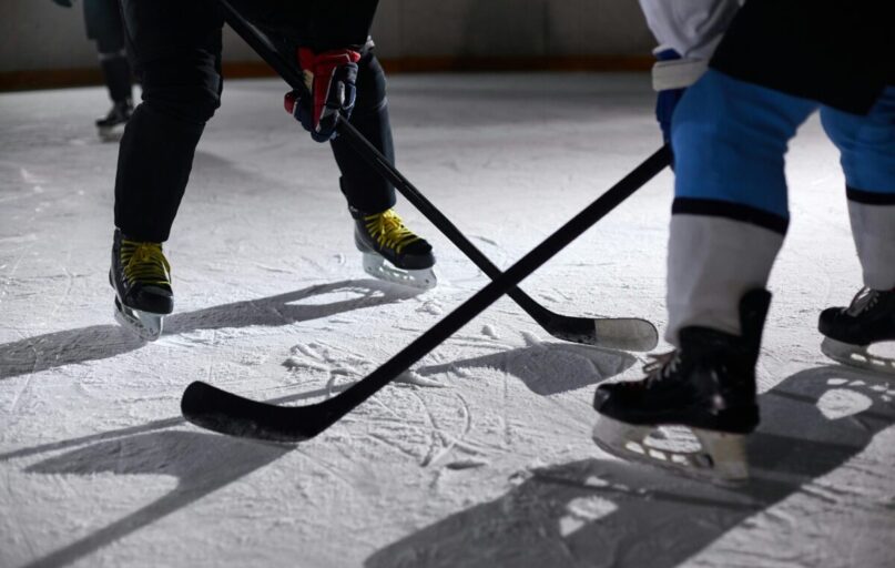 Close-up of hockey players battling for puck during an intense face-off on a lighted ice rink.
