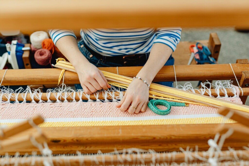 Close-up of hands weaving colorful textile on a wooden loom indoors, showcasing handmade craftsmanship.