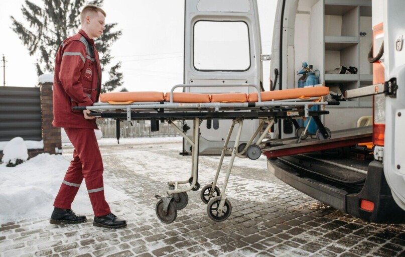 A paramedic loads a stretcher into an ambulance on a snowy day, showcasing emergency response readiness.