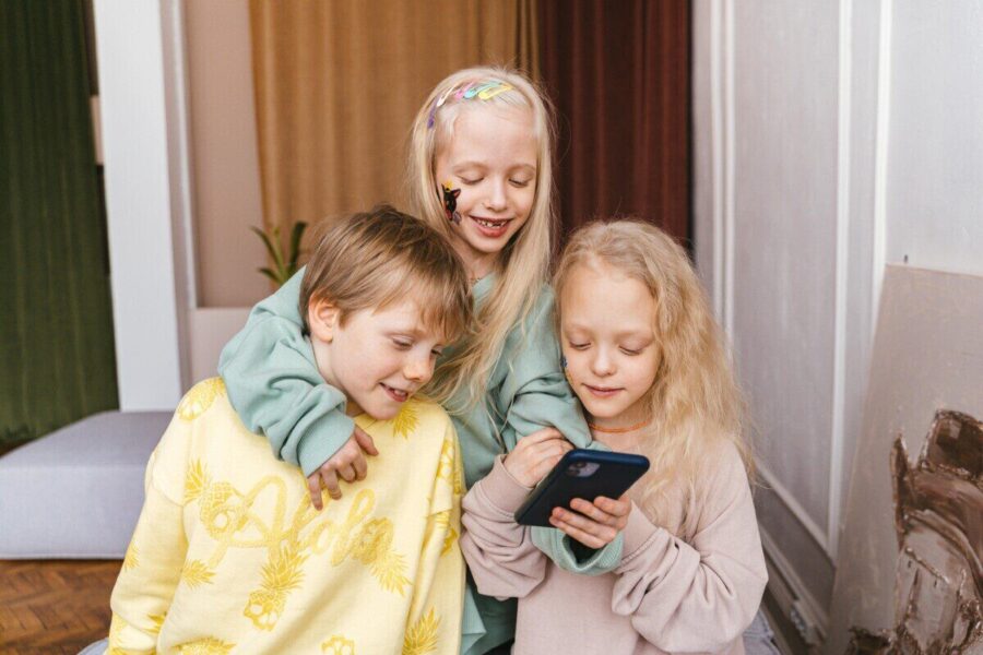 Three children indoors sharing a fun moment with a smartphone, displaying joy and togetherness.