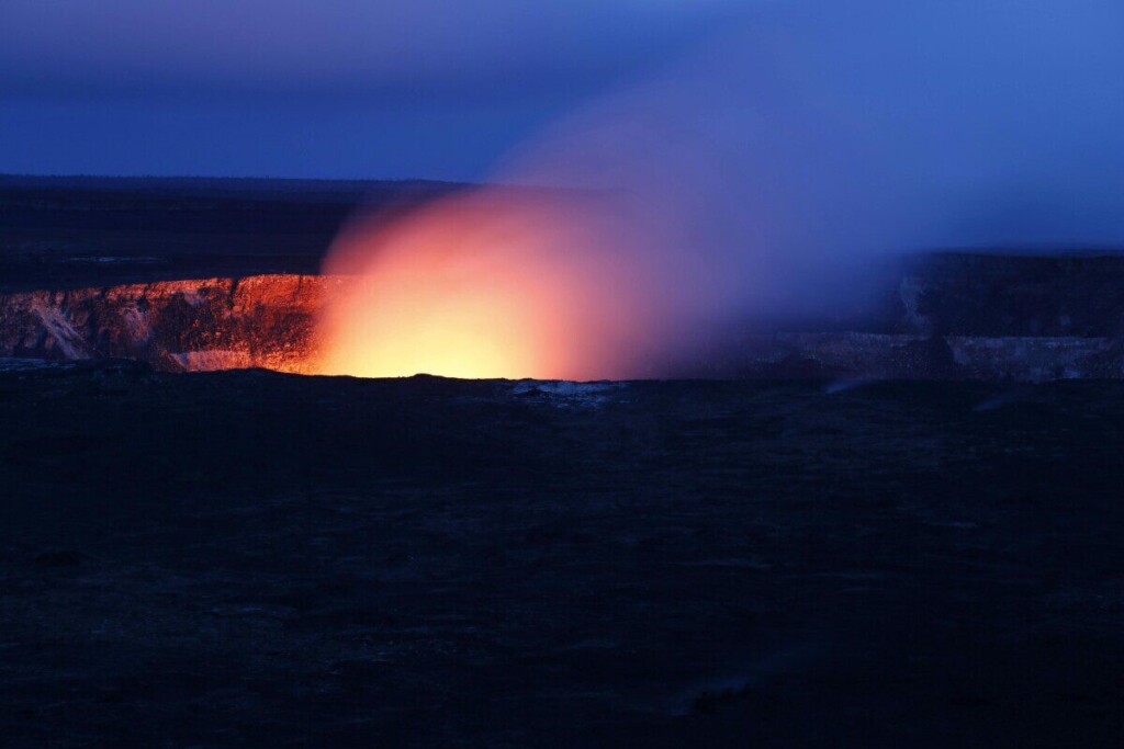 A stunning nighttime view of a volcano eruption, with fiery lava glowing against the dark sky.