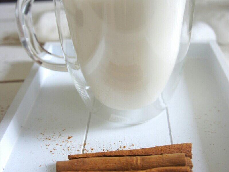 A glass mug of warm milk with cinnamon on a white tray, creating a cozy morning vibe.
