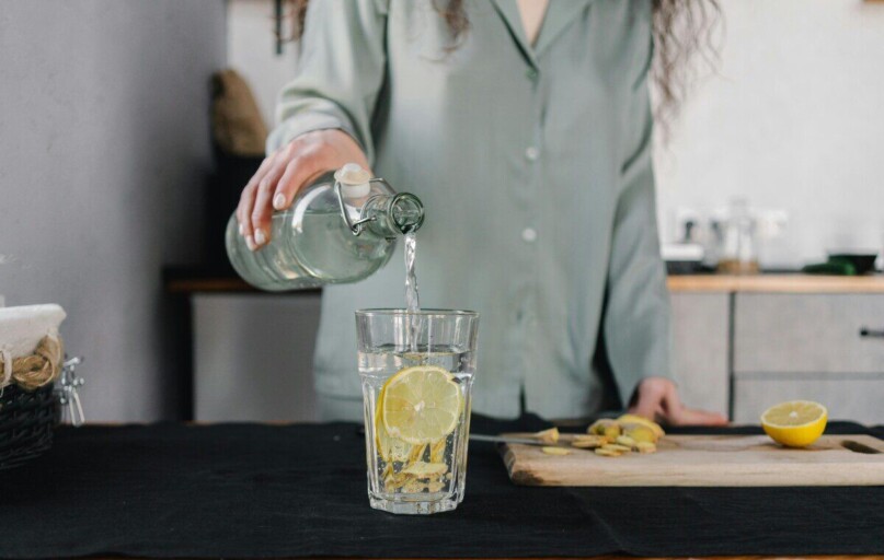 Woman pours water for lemon ginger infusion, promoting health and hydration.