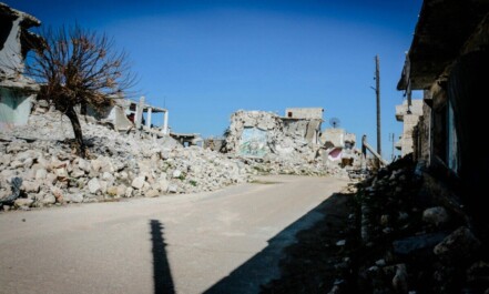 Destroyed buildings and rubble in a deserted street of Idlib, Syria, under clear blue sky.