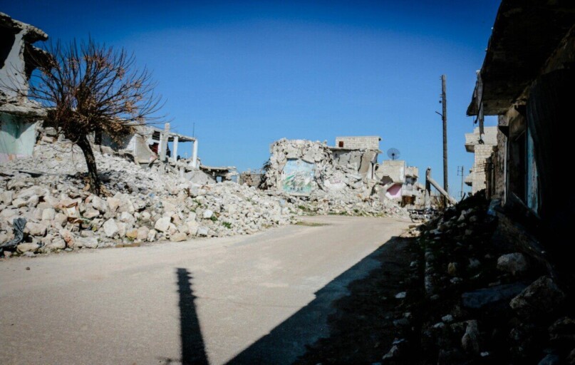 Destroyed buildings and rubble in a deserted street of Idlib, Syria, under clear blue sky.