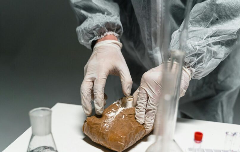 Lab worker analyzes powdered substance in a laboratory setting using safety gear.