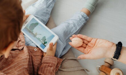 Young child engrossed in a smartphone video while holding a brain model indoors.