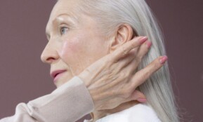 Profile of a senior woman with long grey hair, touching her hair in a serene pose.