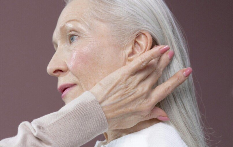 Profile of a senior woman with long grey hair, touching her hair in a serene pose.