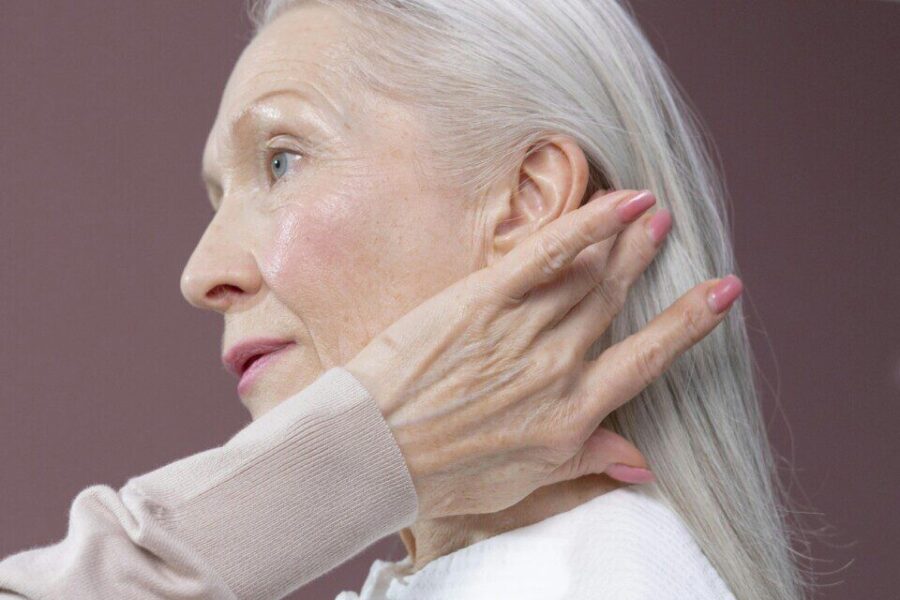 Profile of a senior woman with long grey hair, touching her hair in a serene pose.