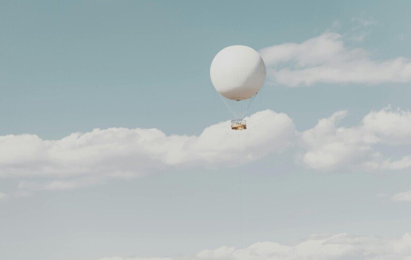 A single hot air balloon drifts peacefully among fluffy clouds in a clear sky.