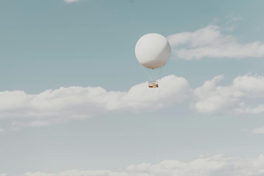 A single hot air balloon drifts peacefully among fluffy clouds in a clear sky.