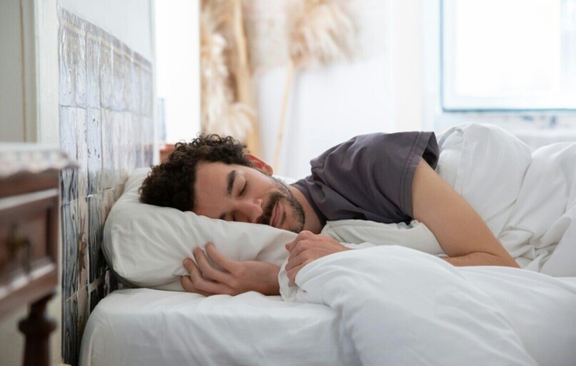 Man resting peacefully in bed, wrapped in white sheets, creating a serene and cozy atmosphere.