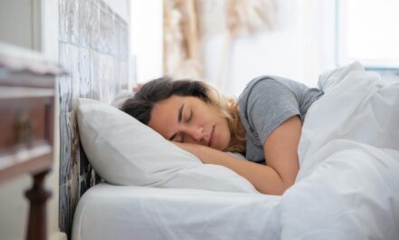 A serene woman sleeps comfortably in bed, surrounded by soft white linens in a sunlit room.