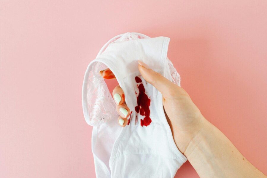 Close-up of a hand holding white underwear with menstrual stain against pink background, highlighting health awareness.