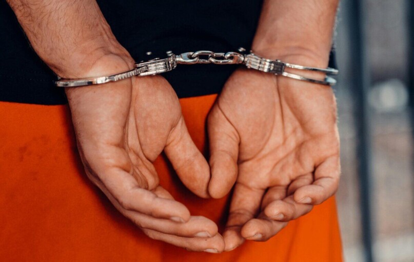 Rear view of handcuffed person in orange uniform, highlighting law enforcement and justice themes.