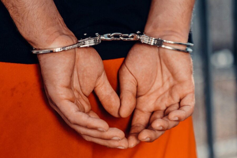 Rear view of handcuffed person in orange uniform, highlighting law enforcement and justice themes.