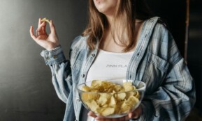 Woman in plaid shirt holding a bowl of potato chips indoors. Casual lifestyle image.