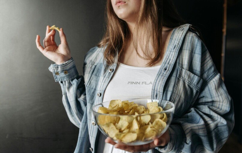Woman in plaid shirt holding a bowl of potato chips indoors. Casual lifestyle image.