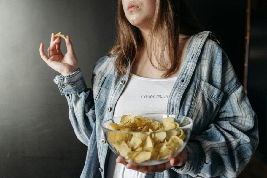 Woman in plaid shirt holding a bowl of potato chips indoors. Casual lifestyle image.
