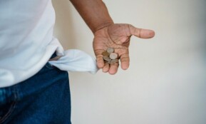A close-up of a person holding coins with a turned-out empty pocket, illustrating financial struggle.
