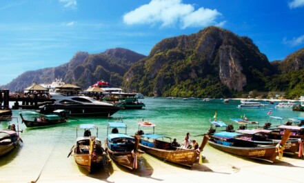 Colorful long-tail boats docked against a mountainous backdrop in Ao Nang, Thailand.
