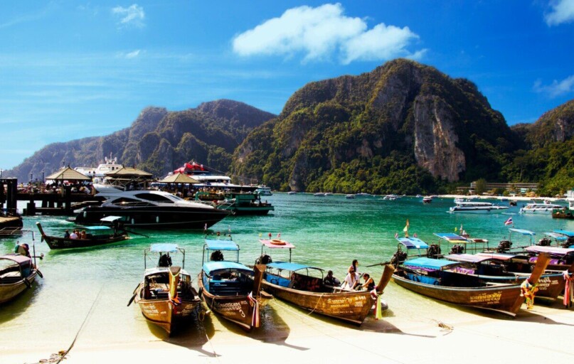 Colorful long-tail boats docked against a mountainous backdrop in Ao Nang, Thailand.