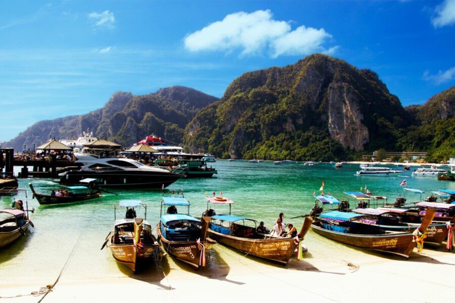 Colorful long-tail boats docked against a mountainous backdrop in Ao Nang, Thailand.