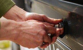 Close-up of hands unlocking a vehicle trunk with a key, showing detail and reflection.