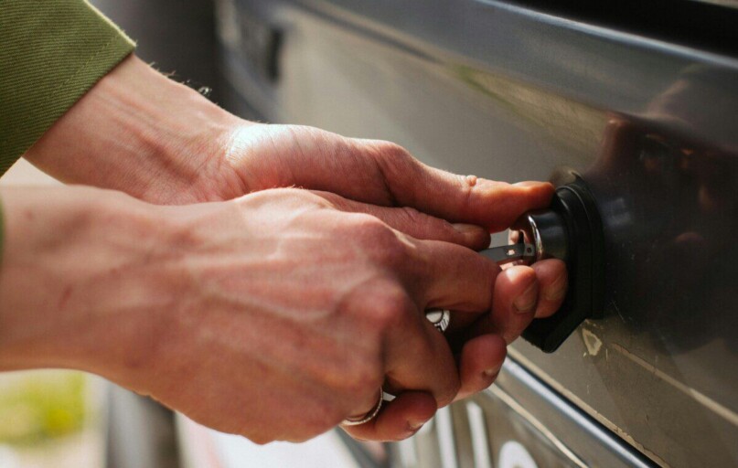 Close-up of hands unlocking a vehicle trunk with a key, showing detail and reflection.