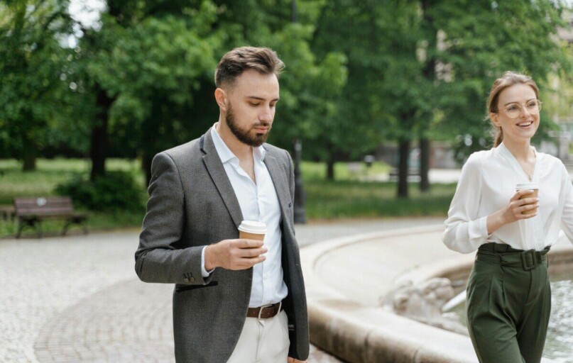 A man and woman in business attire enjoying coffee in a park setting.