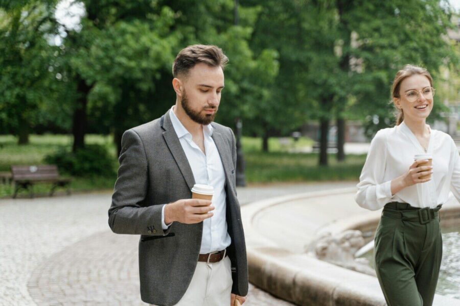 A man and woman in business attire enjoying coffee in a park setting.