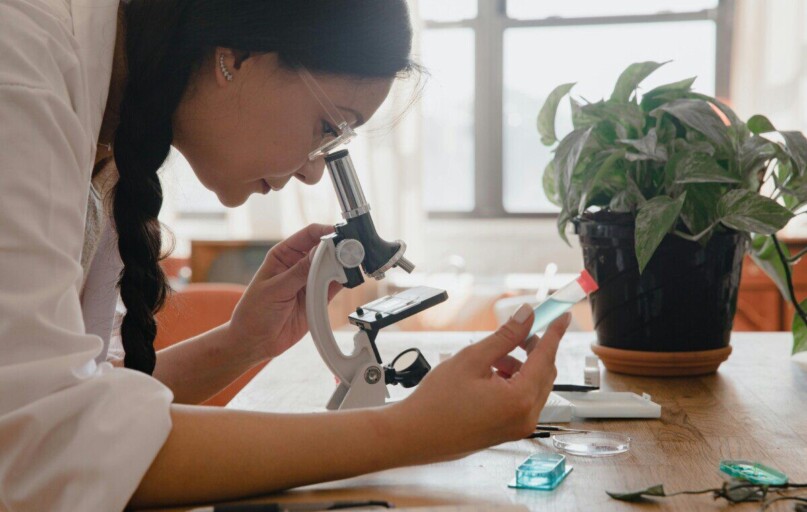 Woman examining sample under microscope in a lab, emphasizing research.