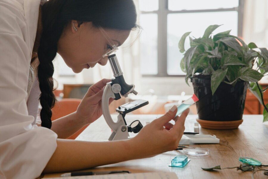 Woman examining sample under microscope in a lab, emphasizing research.