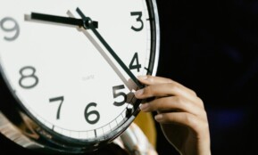 A hand adjusting the time on a large analog clock with bold numbers.