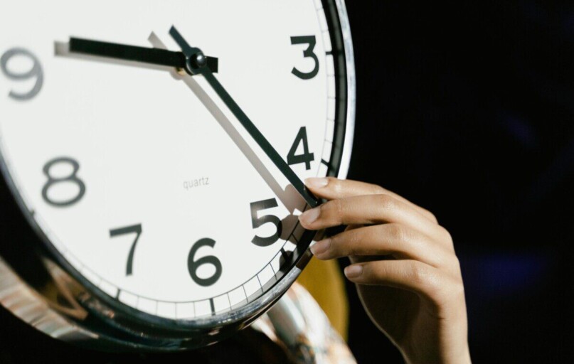 A hand adjusting the time on a large analog clock with bold numbers.